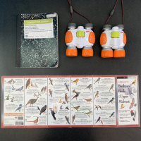 The image of this curiosity kit includes two binoculars, a notebook, and birding guides.